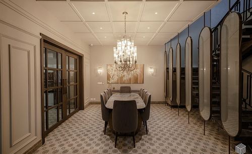 Formal dining room with crystal chandelier, marble table, patterned floor and mirrored oval screen near staircase