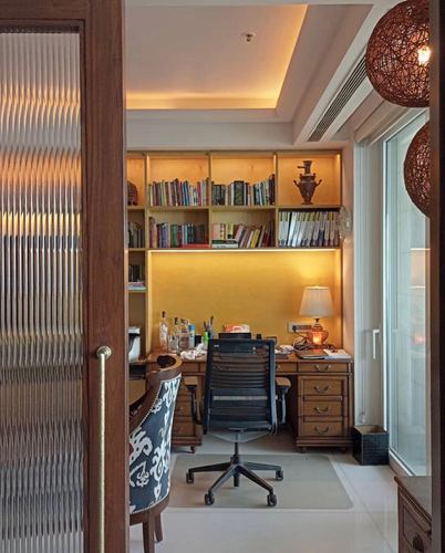 Study nook with built-in bookshelves, wooden desk, office chair, seen through a reeded glass door