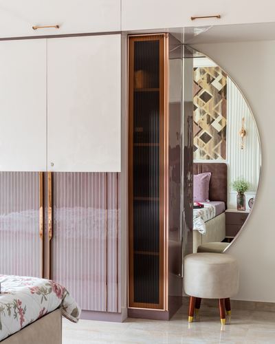 Pink wardrobe with fluted glass insert beside round mirror reflecting a bedroom nook