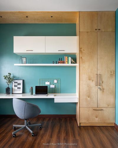 Home office nook with teal wall, floating white desk, wood wardrobe, and grey task chair