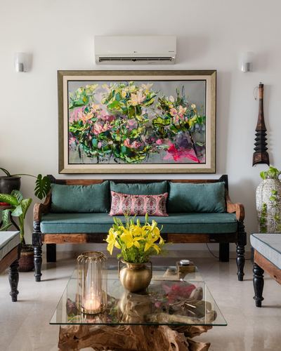 Living room with teal-cushioned wooden sofa beneath a large floral painting and glass coffee table.