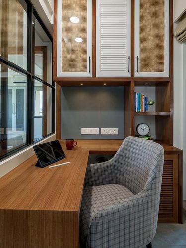 Built-in wooden study desk with cane cabinets above and a plaid armchair beside a window