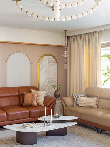 Living room with rust and beige leather sofas, arched marble niches, and a beaded globe chandelier