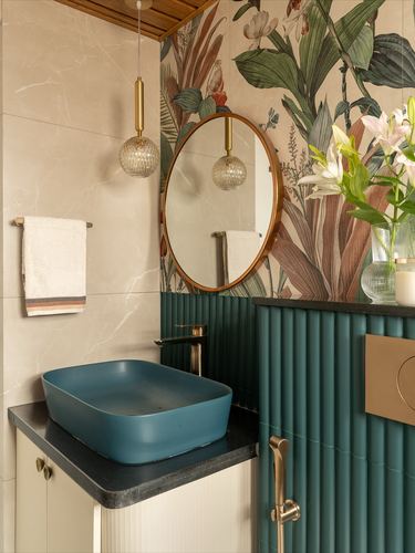 Bathroom vignette with teal vessel sink, round brass mirror, and floral wallpaper