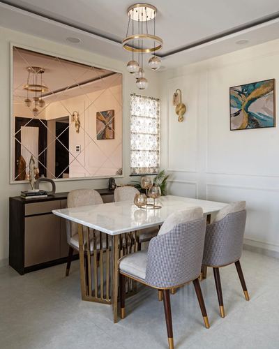 Dining room with marble table, gold-base chairs, mirrored wall panel and layered chandelier