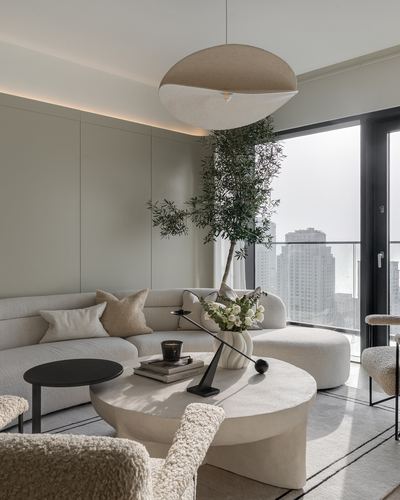 Neutral toned living room with curved boucle sofa, round stone coffee table and city view through floor-to-ceiling windows