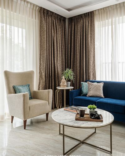 Living room corner with wingback chair, navy sofa, and round marble coffee table by curtained windows