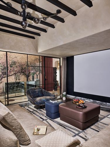 Living room with beamed ceiling, projector screen, marble floor, leather ottomans, and steel-framed glass wall