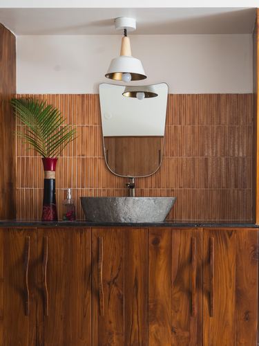 Wood-panelled bathroom vanity with stone vessel sink, arched mirror and pendant light
