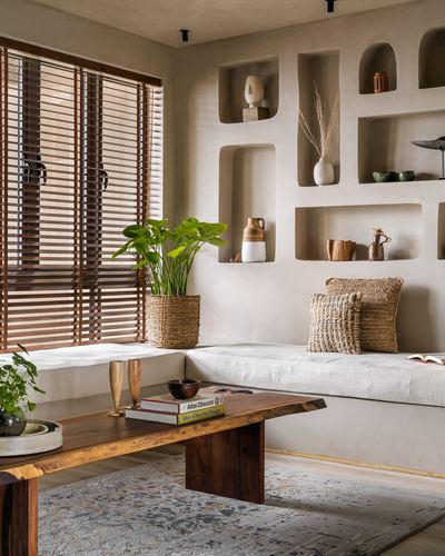 Living room bench seating beneath curved plaster niches with wooden blinds and live-edge coffee table