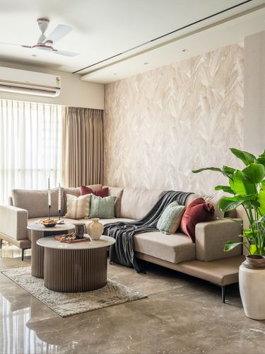 Beige sectional sofa in a Mumbai living room with a textured feather-pattern accent wall and layered round coffee tables