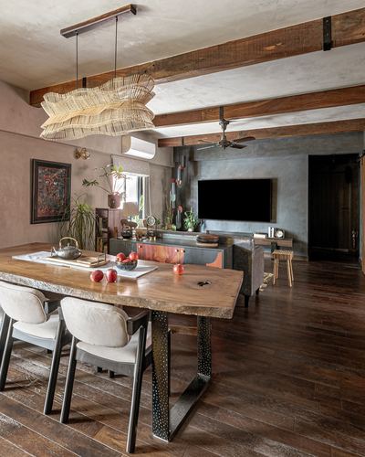 Open dining and living space with live-edge wood table, woven pendant light, exposed beams, and concrete wall.