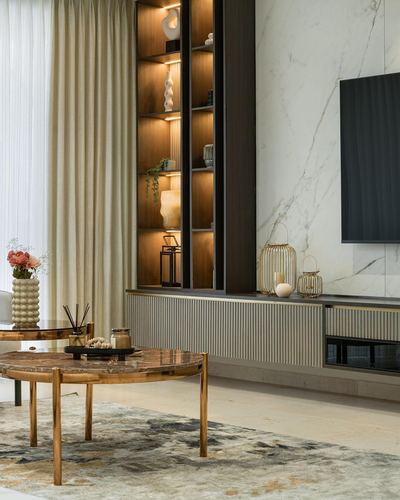 Living room with marble tv wall, fluted cabinetry, lit display niches and brass coffee table