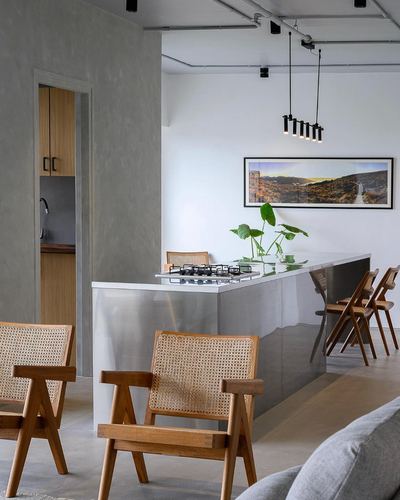 Minimal kitchen island with cane chairs, exposed ceiling pipes, and a framed landscape photo on the wall