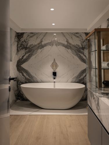 Freestanding oval tub against a mirrored book-matched marble wall with wooden flooring