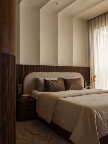 Bedroom with ribbed wood headboard wall, beige bedding, and sheer curtained window