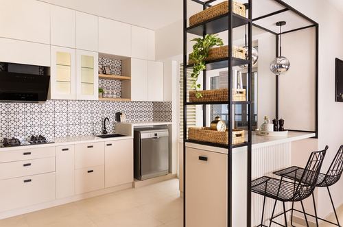 White kitchen with patterned tile backsplash and black metal shelving unit dividing space from bar seating