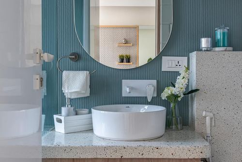 Bathroom vanity with round white sink, oval mirror on ribbed teal wall, terrazzo counter.
