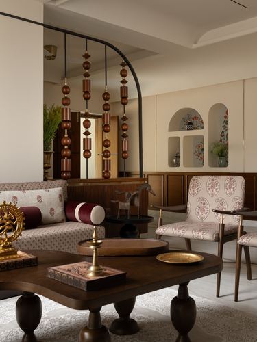Living room with brass Nataraja idol, wooden bead pendant chandelier, floral armchair, and arched wall niches