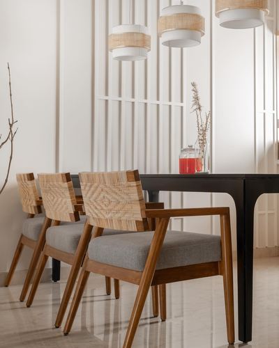 Cane-backed wooden dining chairs beside black table under rattan pendant lights, fluted wall panels behind