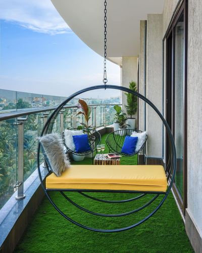 Large circular hanging swing with yellow cushion on turf-floored balcony overlooking city