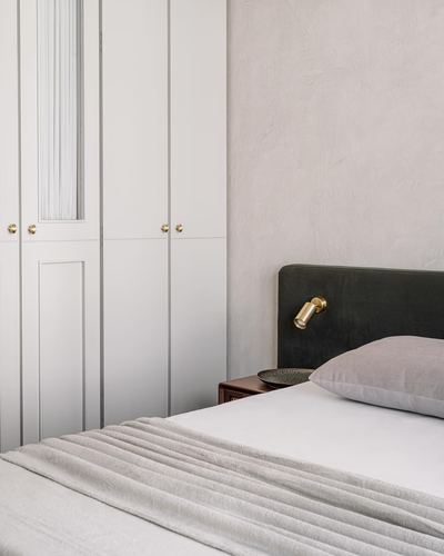 Bedroom corner with fluted wardrobe, plaster wall, olive velvet headboard and brass reading light