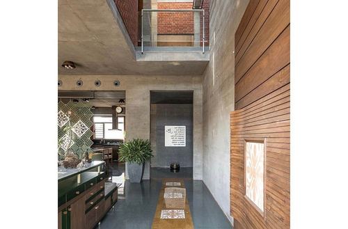 Double-height concrete foyer with wood cladding, brick mezzanine, green cabinetry and plant