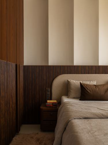 Bedroom corner with fluted wood paneling, curved beige headboard, and dark wood nightstand with books