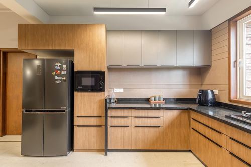 Modern L-shaped kitchen with wood cabinetry, dark stone counters, and steel refrigerator
