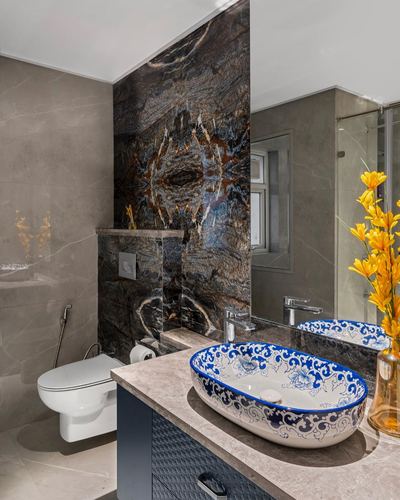 Luxury bathroom with dark bookmatched stone wall, blue and white patterned vessel sink and wall-mounted toilet.