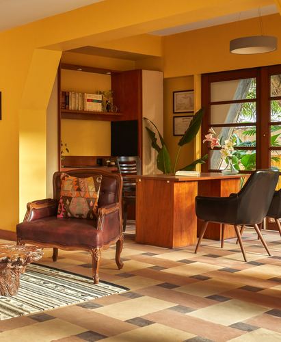 Sunlit study with mustard walls, wooden desk, leather chairs, and patterned tile floor