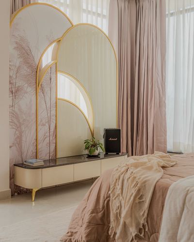 Blush bedroom corner with layered gold-framed arched mirrors above a cream console