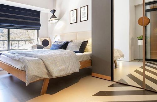 Minimalist bedroom with wood bed, navy roman blind, and mirrored wardrobe beside grey partition wall