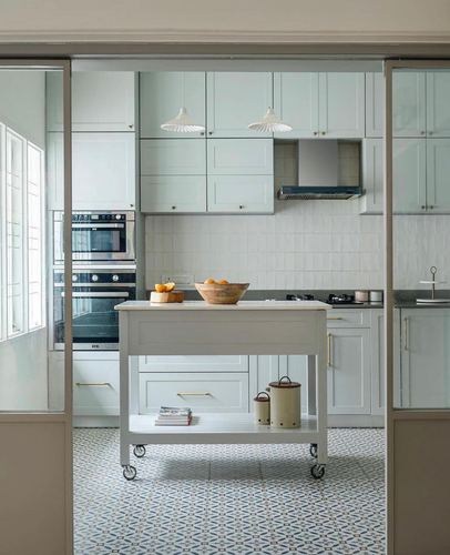 Pale blue kitchen with mobile island, patterned floor tile, and pendant lights over a tiled backsplash