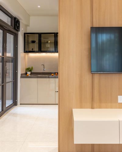 Wood partition with mounted TV beside a view into a compact modern kitchen with glass cabinets