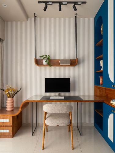 Study nook with glass desk, boucle chair, hanging wooden shelf, and blue arched cabinetry