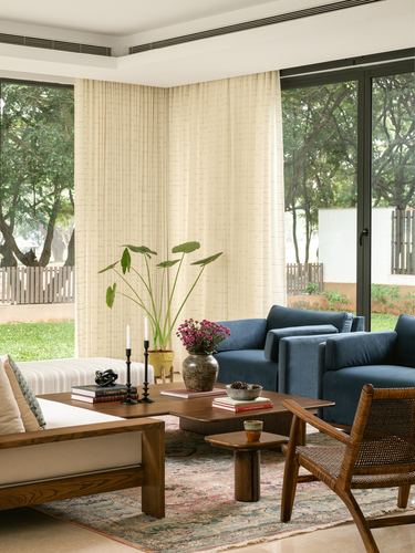 Living room with blue velvet armchairs, wooden coffee table, and sheer curtains framing a garden view