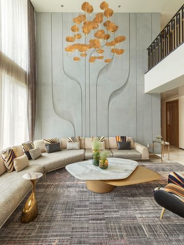 Double-height living room with sculpted grey wall relief, gold leaf chandelier, and curved beige sectional