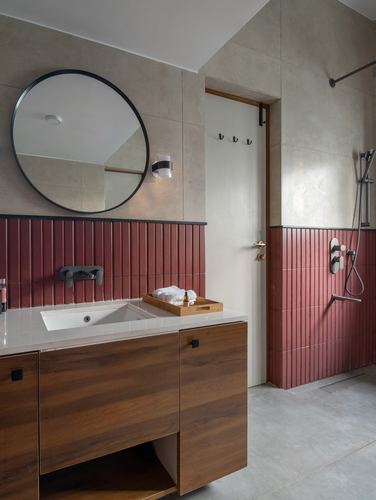 Bathroom with round black mirror, wood vanity, and ribbed terracotta tile wainscot