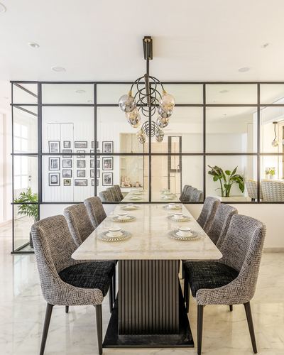 Dining table with marble top and fluted black base under a spherical chandelier, framed by a black steel-glass partition