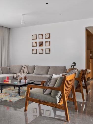 Minimalist living room with grey sectional, wooden armchairs, marble floor and framed wall grid
