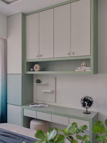 Sage green and white study nook with wall cabinets, open shelf, desk, and globe decor