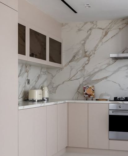 L-shaped kitchen with beige cabinetry and veined marble backsplash and countertop