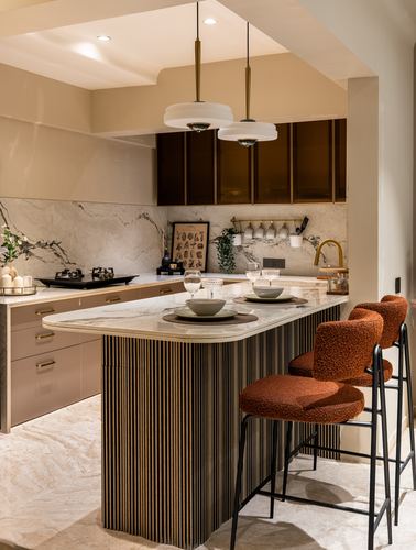 Kitchen island with fluted wood base, marble top and rust bouclé bar stools under twin pendants