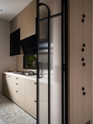 Beige kitchen with black chimney hood, fluted glass sliding door, and terrazzo flooring