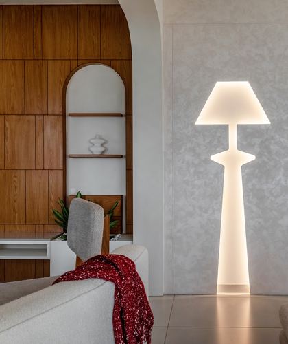 Glowing sculptural floor lamp beside textured wall, arched wooden niche and boucle sofa with red throw
