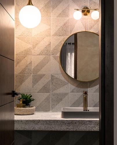 Bathroom vignette seen through doorway with round brass mirror, terrazzo counter and glowing globe pendant