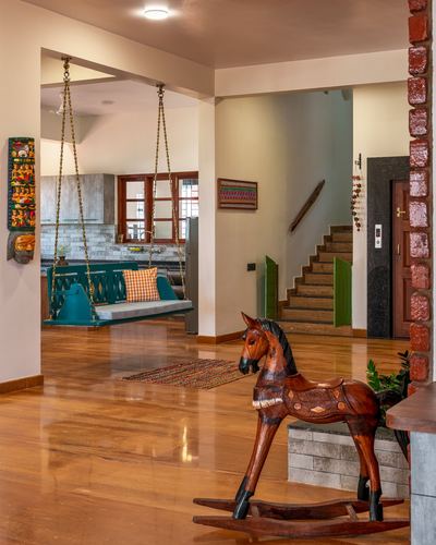 Foyer with wooden rocking horse, glossy stone floor, teal swing and staircase beyond