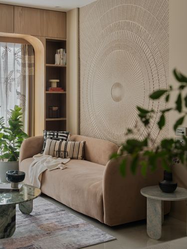 Beige curved sofa against a circular textured wall panel beside a wooden shelving nook and marble side tables.