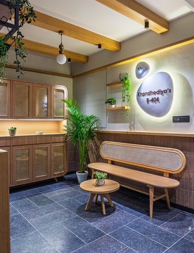 Foyer with cane bench, wood beams, and backlit nameplate wall reading Khandhediya's B-404